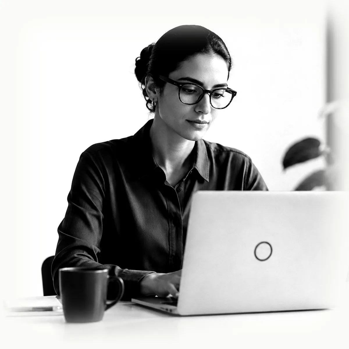 A woman at a bright desk, focused on her laptop.